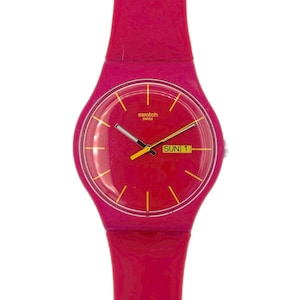 Puede incluir: Un reloj Swatch de color rosa brillante con una correa a juego. La esfera del reloj también es rosa con marcadores de hora y agujas amarillas. El día de la semana, "SUN 1", se muestra en un cuadro amarillo. La palabra "swatch swiss" está impresa en la esfera.
