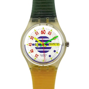 Può includere: Un orologio Swatch vintage con cassa in plastica trasparente e cinturino bicolore. Il quadrante è bianco con dettagli rossi, gialli e verdi, incluso il giorno della settimana. Le lancette dell'orologio sono rosse e verdi.