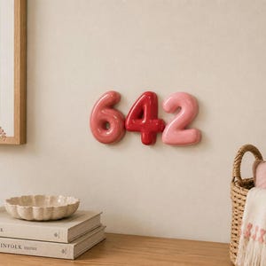 May include: Three dimensional wall mounted numbers 6, 4, and 2. The number 6 is a muted rose colour, the number 4 is a vibrant cherry red, and the number 2 is a soft pastel pink. Each number has a smooth, glossy, rounded finish and a puffy shape.