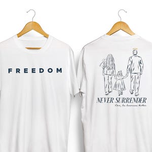 May include: White t-shirts with the word "FREEDOM" in navy blue on the front. The back of the shirt features a line drawing of a family with the text "NEVER SURRENDER" and "Love, an American Mother."
