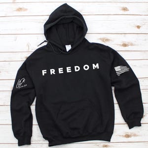 A black hoodie with the word "FREEDOM" printed on it, laid out on a wooden surface.