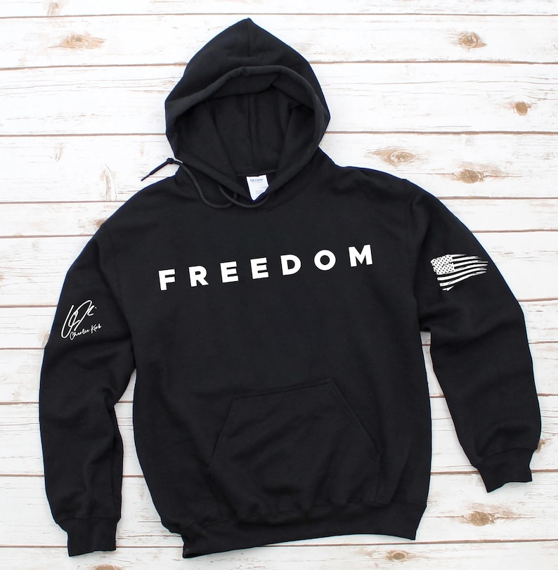 A black hoodie with the word "FREEDOM" printed on it, laid out on a wooden surface.