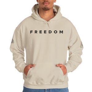 A man wearing a beige hoodie with the word "FREEDOM" printed on it.