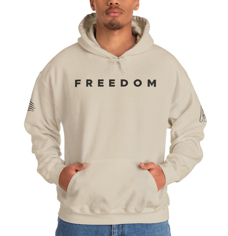 A man wearing a beige hoodie with the word "FREEDOM" printed on it.