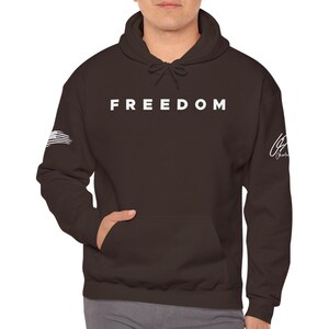 A person wearing a dark brown hooded sweatshirt with the word "FREEDOM" printed on it.