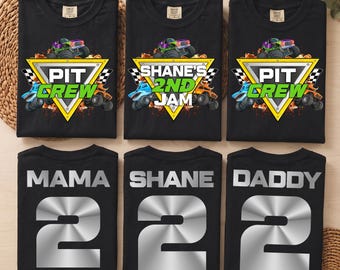 May include: Six black t-shirts arranged in two rows. The top row features monster truck graphics with text reading PIT CREW or SHANE'S 2ND JAM. The bottom row displays silver text reading MAMA, SHANE, or DADDY above a large silver number 2.
