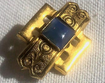 Broche Freirich de estilo renacentista en tonos dorados con esmalte negro y cristal azul