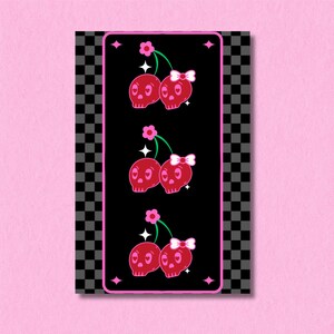 May include: A vertical print featuring three sets of red skull cherries with pink bows and green stems on a black background. The print is framed by a pink border with star accents and a black and gray checkered pattern.