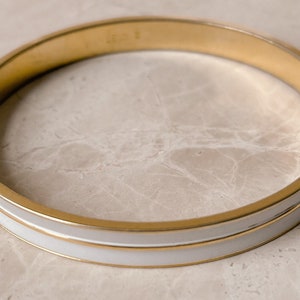 Może przedstawiać: Złota bransoletka typu bangle z białym paskiem emaliowanym.