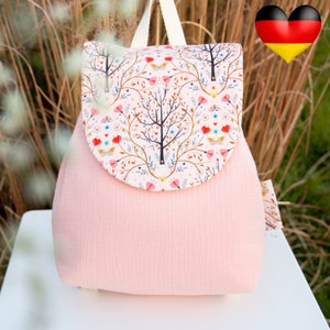 May include: A pink backpack with a flap featuring a colourful floral pattern. The flap has a rounded top and is secured with a white strap. The backpack has a small pocket on the side.