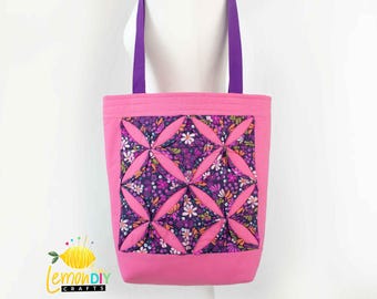 May include: Pink tote bag with purple straps and a quilted floral design. The design features a repeating pattern of pink and purple flowers on a dark purple background.