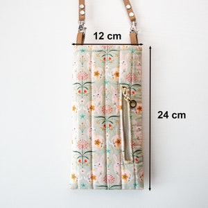 May include: A green quilted phone pouch with a zipper closure and a bunny rabbit print. The pouch has a brown leather strap with silver hardware. The pouch measures 12 inches by 24 inches.
