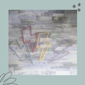 May include: Five lightning bolt shaped wall decor pieces made of rope in various colours including yellow, blue, pink, and red. The decor is displayed on a wood background.