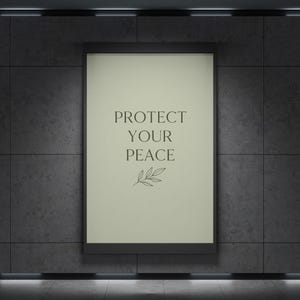 May include: A framed poster with the words "PROTECT YOUR PEACE" in a dark font, with a small leaf design below the text. The poster is set against a dark gray tiled wall.