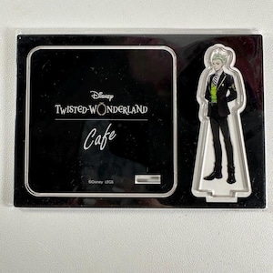 May include: A black acrylic display featuring the "Disney Twisted-Wonderland Cafe" logo. A clear acrylic figure of a character in a black suit and green accents stands to the right. The display is rectangular.