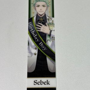 May include: A bookmark featuring a green-haired anime character wearing a white suit with a black sash that says "Birthday Boy". The character is smiling and holding his hand to his chest. The bookmark also has the character's name, "Sebek", printed on it. The text "© Disney Aniplex Inc. NOT FOR SALE" is printed at the bottom of the bookmark.