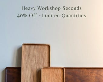 May include: A collection of rectangular and oval wooden trays in various shades of light and dark brown wood grain. The text "Heavy Workshop Seconds 40% Off · Limited Quantities" is printed in dark gray above the wooden trays against a light background.