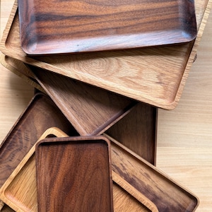 May include: A collection of rectangular wooden trays in various shades of brown. The trays are stacked and arranged, showcasing the natural wood grain and textures. The trays have slightly raised edges.