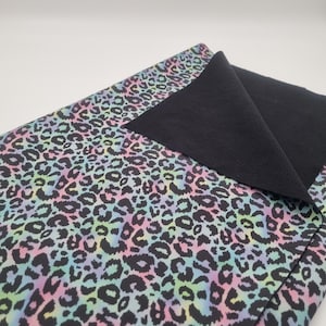 Könnte beinhalten: Gefalteter Stoff mit einem Leopardenmuster in Pastellfarben aus Rosa, Blau und Gelb auf schwarzem Hintergrund. Die Rückseite ist einfarbig schwarz. Geeignet für Kleidung oder Bastelarbeiten.