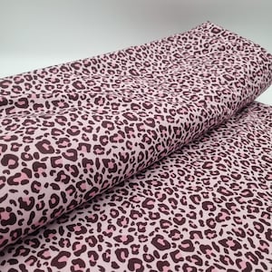 Könnte beinhalten: Rosa Stoff mit Leopardenmuster. Der Stoff hat dunkelbraune Flecken mit rosa Zentren auf einem hellrosa Hintergrund. Der Stoff ist gefaltet und zeigt das Muster im Detail. Geeignet für verschiedene Nähprojekte.
