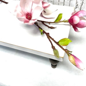 May include: A white wooden pedestal with a pink magnolia flower arrangement. The pedestal has turned wooden legs and a white painted surface.