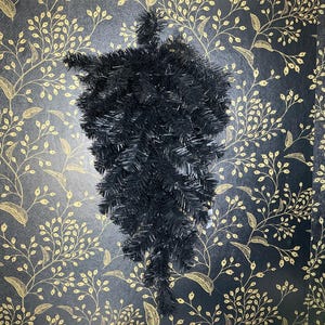 May include: A teardrop-shaped artificial evergreen swag featuring dense, solid black pine needles. The decorative piece has a tapered design with a full, bushy texture, constructed from synthetic materials that mimic the appearance of natural pine branches.