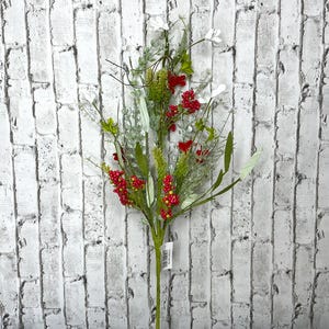 May include: A decorative floral stem featuring a mix of greenery, white flowers, and vibrant red berries. The artificial arrangement has a natural look, perfect for adding a touch of color and texture to any space. The stem is set against a white brick wall.
