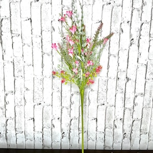 May include: A bundle of artificial flowers with pink blossoms, red berries, and green foliage. The stems are green, and the arrangement is set against a white brick wall.