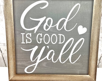 Könnte beinhalten: Ein gerahmtes Schild mit grauem Hintergrund und weißen Buchstaben, auf dem "God is good y'all" mit einem kleinen weißen Herz steht.