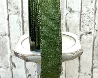 Puede incluir: Un carrete de cinta verde con un acabado brillante. La cinta está envuelta alrededor de un carrete plateado y está sentada sobre un pedestal blanco.