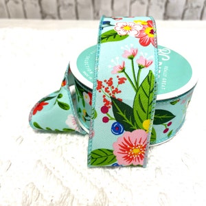 May include: A roll of light blue floral ribbon with a colorful flower pattern. The ribbon features pink, red, yellow, and white flowers with green leaves. The ribbon is on a white surface.