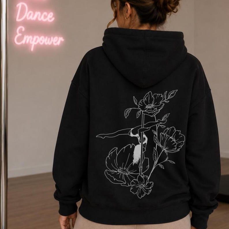 May include: A black hooded sweatshirt featuring a white line art graphic on the back. The design depicts a person performing a pole dance move integrated with large floral illustrations. The hoodie has long sleeves and a hood with a drawstring.