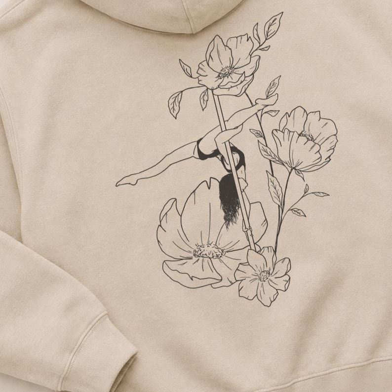 May include: A beige hooded sweatshirt featuring a black line art graphic on the back. The illustration depicts a person performing a pole dance move on a vertical pole, surrounded by large, detailed floral blossoms and leaves.