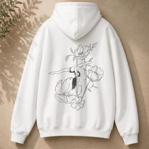 May include: A white hooded sweatshirt featuring a black line art illustration on the back. The graphic depicts a person performing a pole dance move, surrounded by several large, detailed floral blossoms and leaves on long, slender stems.