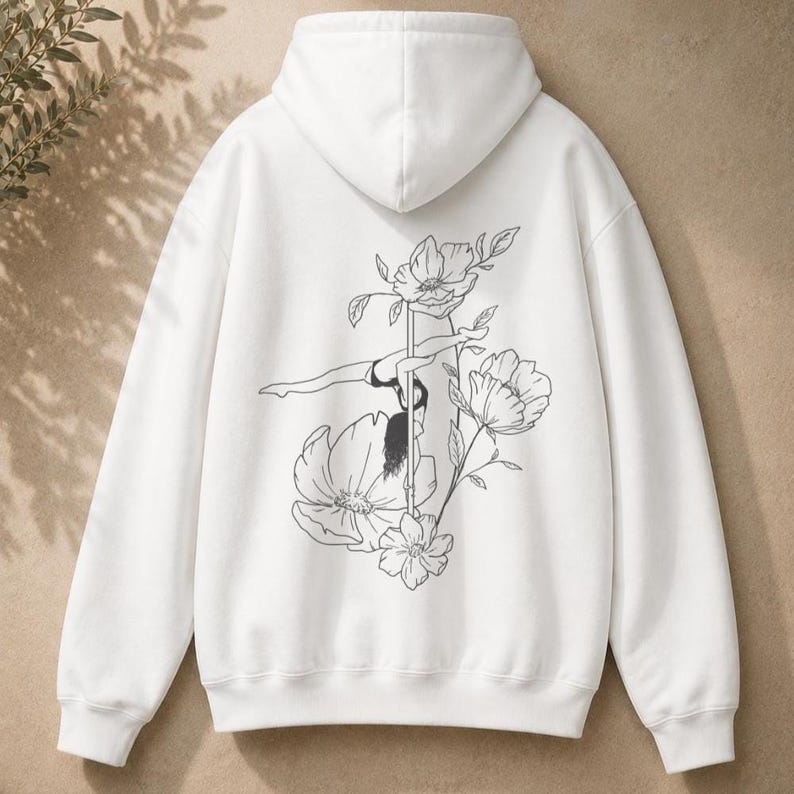 May include: A white hooded sweatshirt featuring a black line art illustration on the back. The graphic depicts a person performing a pole dance move, surrounded by several large, detailed floral blossoms and leaves on long, slender stems.