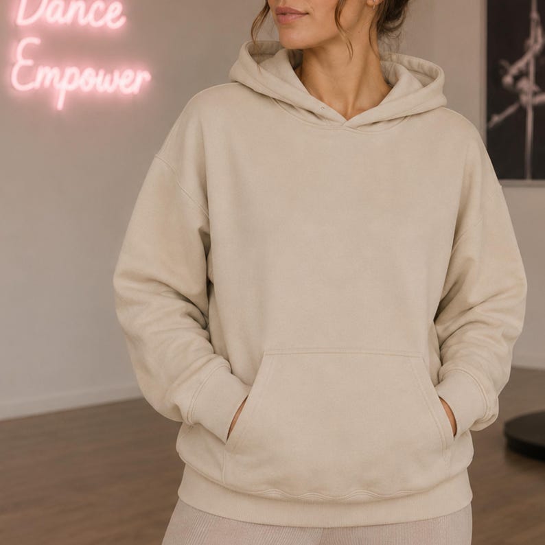 May include: A beige long-sleeve hooded sweatshirt featuring a front kangaroo pocket, ribbed cuffs, and a ribbed hem. The garment is constructed with a relaxed fit, a drawstring-free hood, and a solid neutral color throughout the entire design.