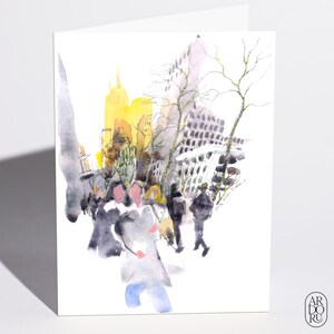 May include: A greetings card featuring a watercolour illustration of a busy city street scene with pedestrians in dark clothing, bare trees, and tall yellow buildings in the background. The text ARDORU is printed in a small circle in the bottom right corner.