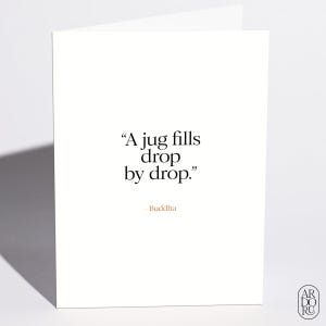 May include: A white greeting card featuring the black text "A jug fills drop by drop." followed by the attribution "- Buddha" in a light orange color. The card is oriented vertically with a clean, simple design and a shadow cast to the left.