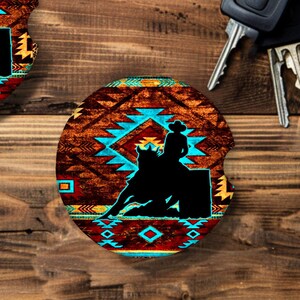 May include: Two round brown, blue, and yellow coasters with a silhouette of a person riding a horse over a barrel. The coasters have a southwestern pattern.