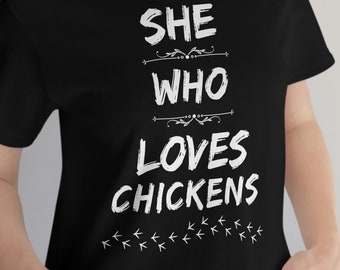 May include: A black t-shirt with white text that reads "She who loves chickens" with a row of white chicken footprints below the text.