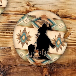 May include: Two round coasters with a southwestern design featuring a geometric pattern in shades of brown, beige, teal, and white. One coaster depicts a cowboy roping a calf, while the other shows a cowboy riding a horse.