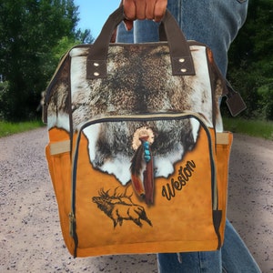 May include: A brown and tan backpack with a faux fur flap and a brown leather handle. The backpack has a zippered pocket on the front and a large compartment with a zipper closure. The backpack has a brown elk silhouette and the name Weston printed on the front.