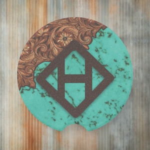 May include: A round turquoise and brown coaster with a geometric design in the center. The design features a brown diamond shape with a brown letter "H" inside.