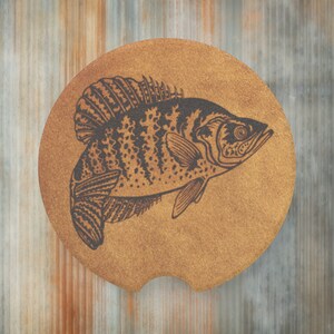 May include: A brown leather coaster with a black and white illustration of a crappie fish.