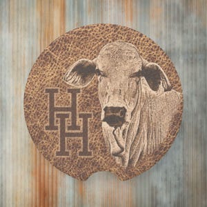 May include: Brown leather coaster with a white cow head and the letters "HHH" in black.