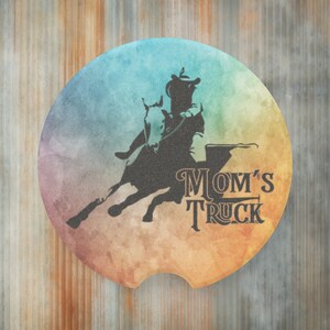 May include: A round, colorful car coaster with a silhouette of a person riding a horse over a barrel. The text "MOM'S TRUCK" is printed below the image.