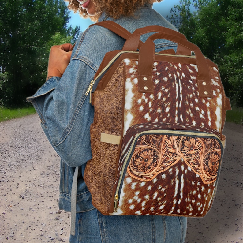 May include: A brown leather backpack with a deer print design. The backpack has a front pocket with a tooled leather design.
