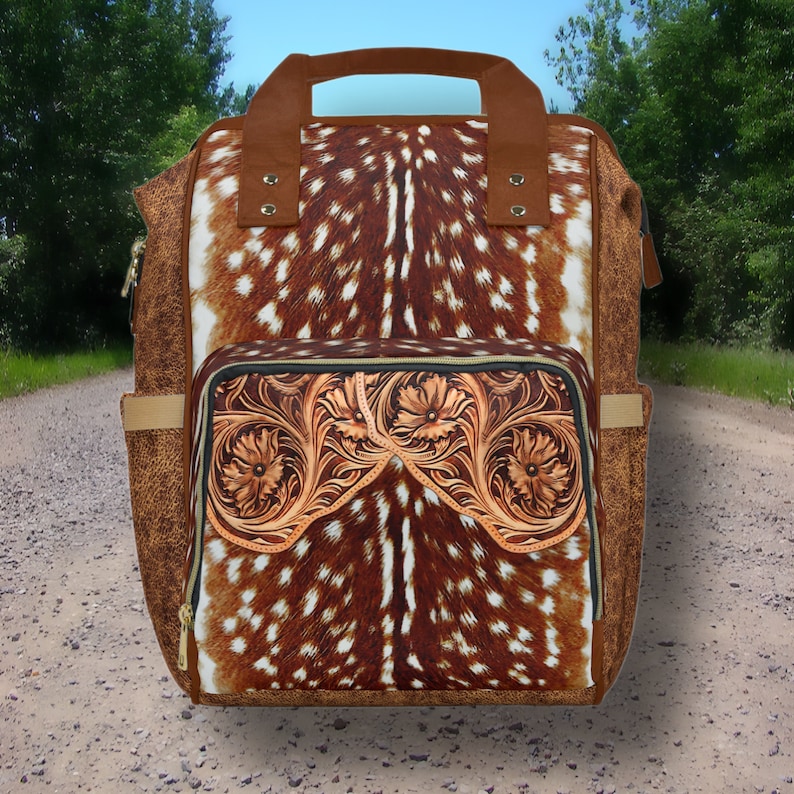 May include: A brown leather backpack with a deer print design and a tooled leather front pocket. The backpack has a top handle and adjustable shoulder straps.