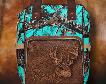 May include: A turquoise and brown camouflage backpack with a brown leather front flap. The flap features a deer head with antlers and the name "Rowdy" embossed in the leather.