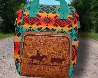 May include: A turquoise and brown backpack with a southwestern pattern and a large front pocket featuring a brown leather-like material with a silhouette of a cowboy riding a horse and a cow.